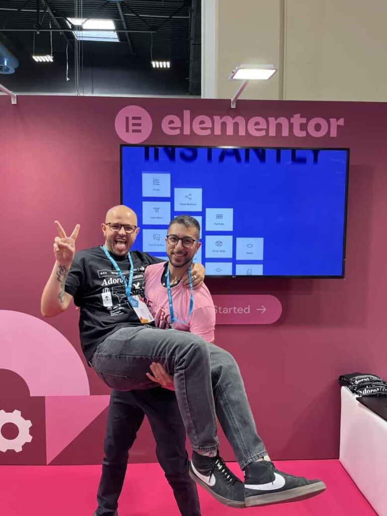Two smiling men posing playfully in front of the Elementor booth sign at a web development conference.
