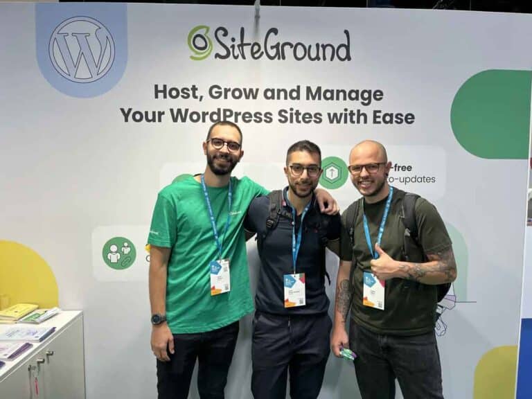 Tre partecipanti alla conferenza sorridono e posano di fronte allo stand di SiteGround, che promuove l'hosting e la gestione di siti WordPress.